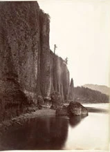 Sepia photograph of a rock cliff above water