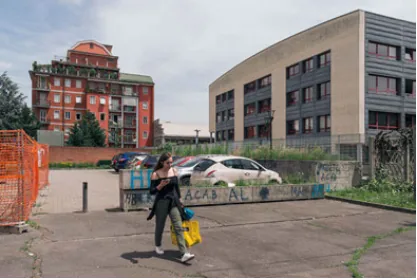 A pedestrian moving between a residential block, a civic building, and a temporarily fenced public edge