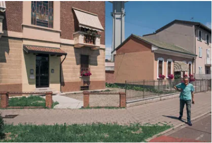 A pedestrian crossing a quiet residential street between modest houses in Pero