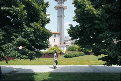 A lone pedestrian walking through a green space framed by mature trees and Pero's water tower