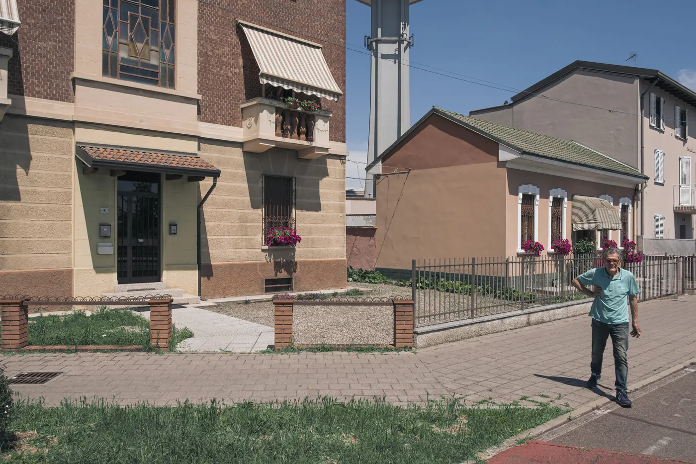 A pedestrian crossing a quiet residential street between modest houses in Pero