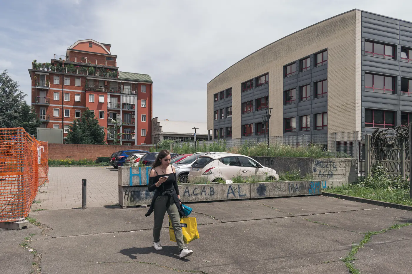A pedestrian moving between a residential block, a civic building, and a temporarily fenced public edge