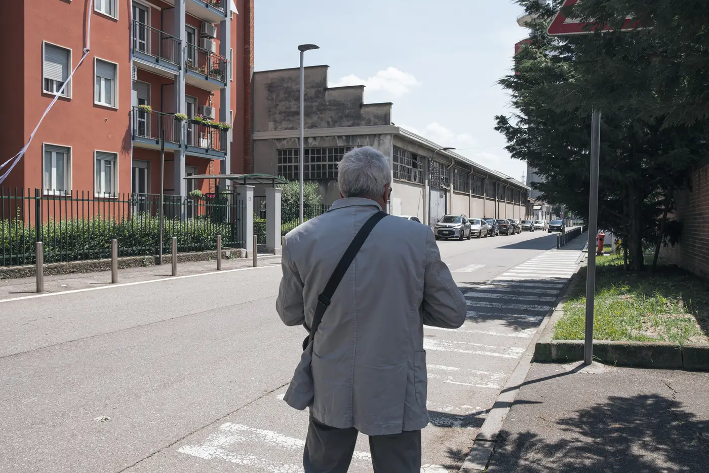 A longtime resident walking down a residential street lined by apartment blocks and industrial buildings