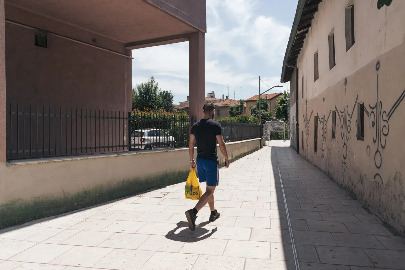 A pedestrian carrying a yellow bag through a covered passage marked with graffiti