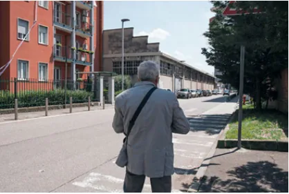 A longtime resident walking down a residential street lined by apartment blocks and industrial buildings