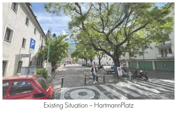 Existing Hartmannplatz beneath mature trees beside parked bicycles and cars