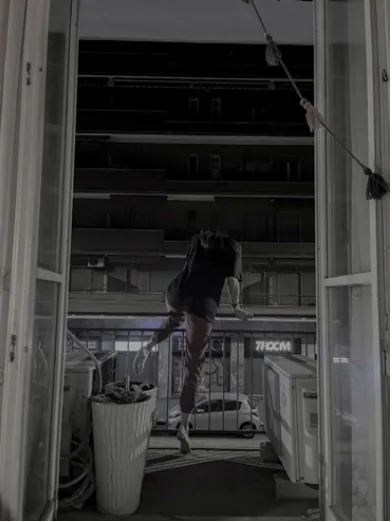 A figure climbing through an open balcony window toward the street