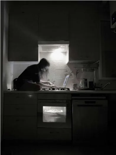 A solitary figure working in a dark kitchen, illuminated by the light above the stove