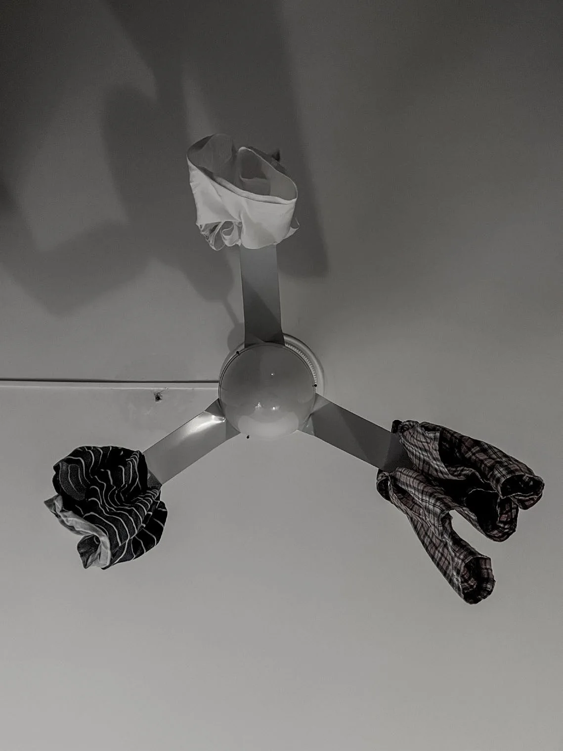 A ceiling fan seen from below with an item of clothing draped over each of its three blades