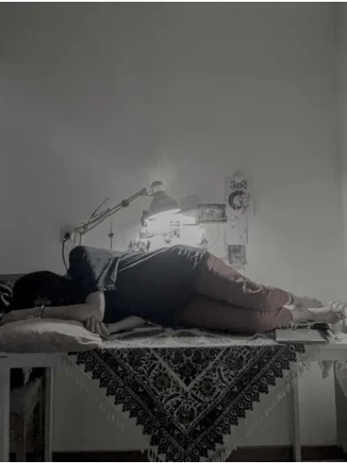 A person lying across a sofa beneath a task lamp in a softly lit room